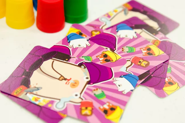 散落在桌面上的紫色动物插画手牌,背景可以看到黄色和红色的小桶