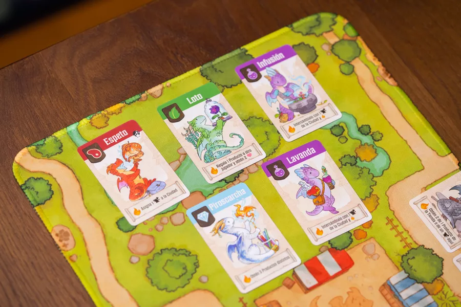 绿色的游戏垫上摆放着各种工匠龙卡牌，如拿着肉串的红龙和带着药水的紫龙