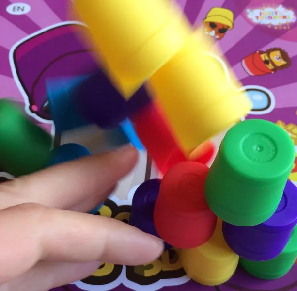 动态瞬间:一只手正在小心翼翼地从彩色小桶金字塔中抽出一只绿色小桶,上方的小桶呈现模糊的晃动感