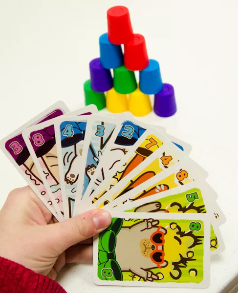 手持一叠彩色数字手牌,背景是由彩色小桶堆叠而成的金字塔