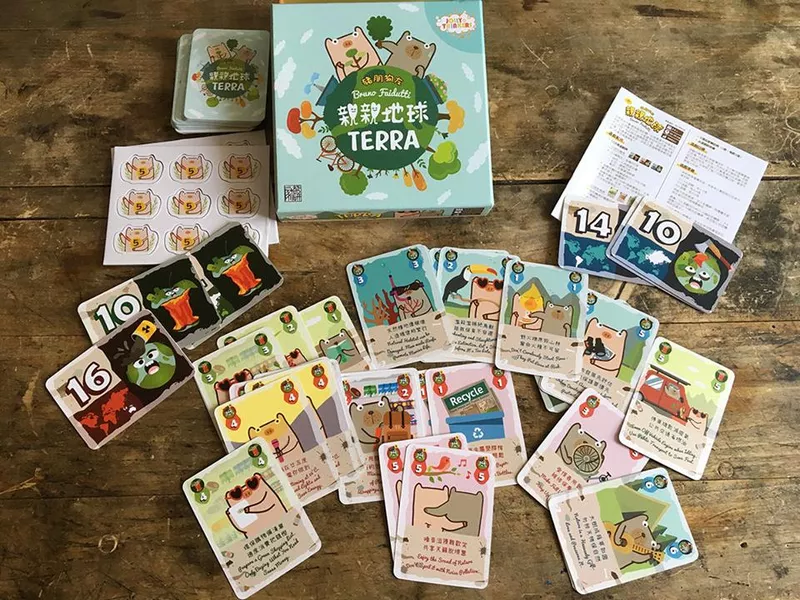 木质桌面上散开的《亲亲地球》实体配件，包装盒与五颜六色的手绘卡牌铺满一桌