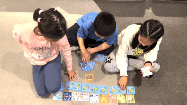 玩耍现场：三个孩子专注地围坐在地毯上，正试图从一堆精美卡牌中整理出正确的逻辑线索